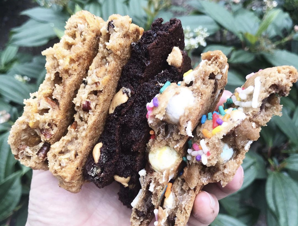 A view of a hand holding chocolate chip cookies split in half from Lowrider Baking Company.