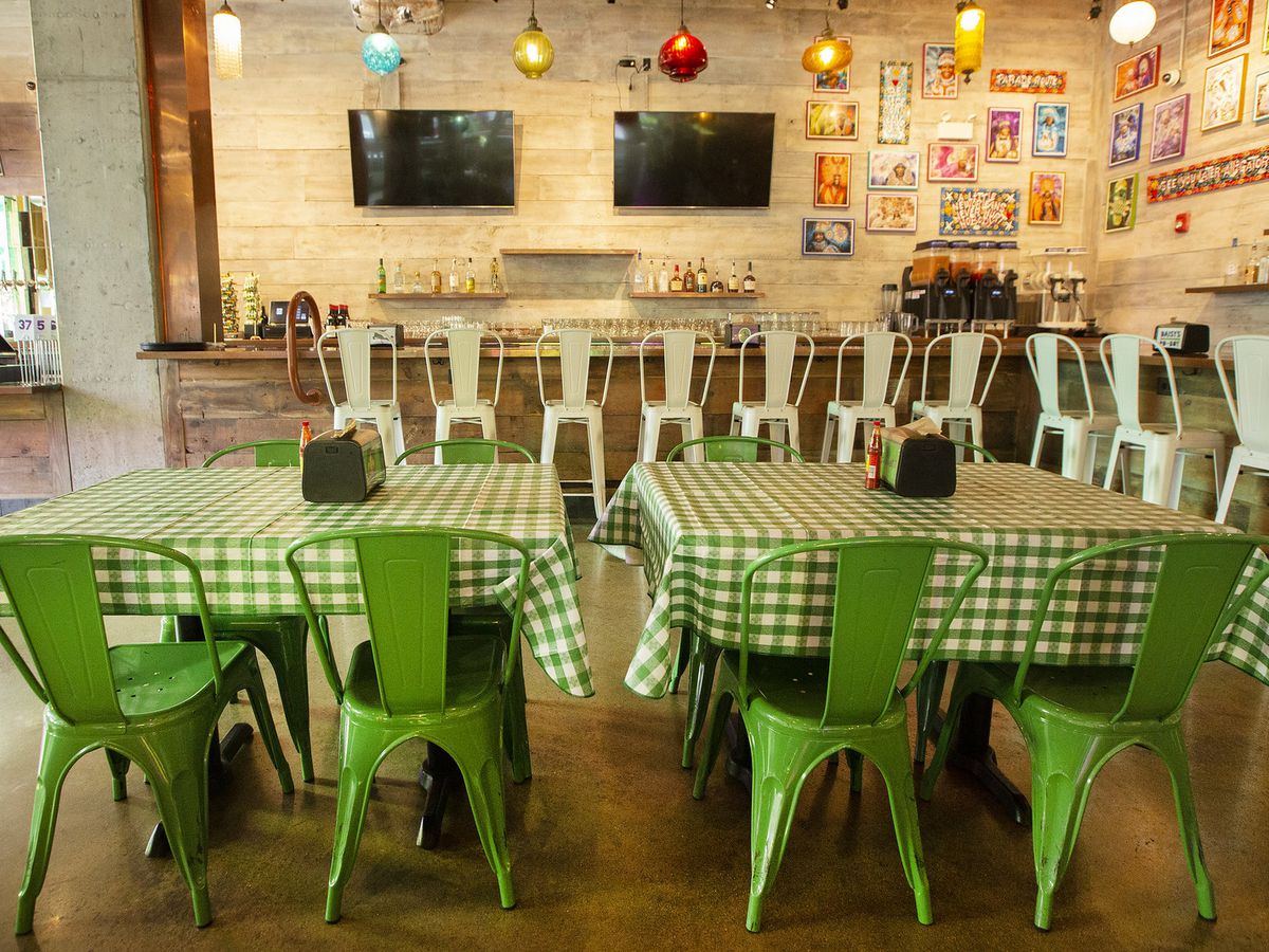 An empty bar with tables with green and white tablecloths.