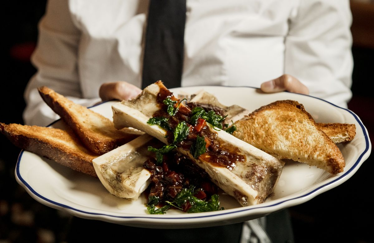 A plate with two bones filled with marrow and topped with a red marmalade, with triangular toasts on either side.