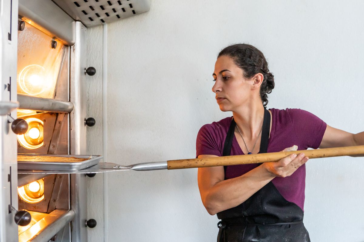 A woman in an apron taking bread out of an oven