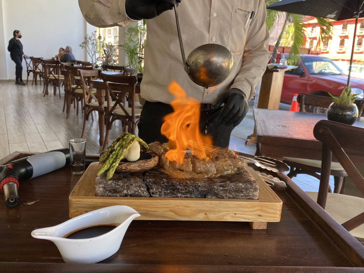A server pours flaming sauce over a steak on a wooden serving board