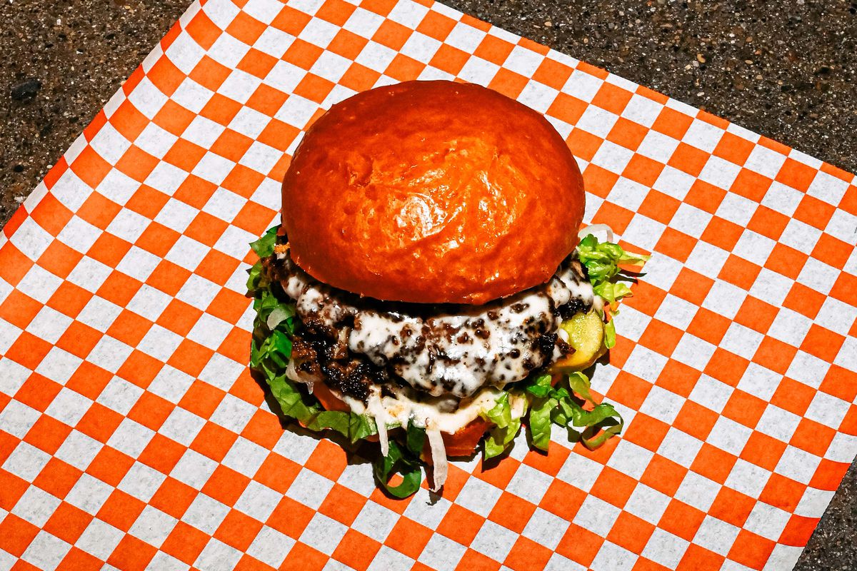 A smash burger with white barbecue sauce rests on a checkered, red and white napkin.