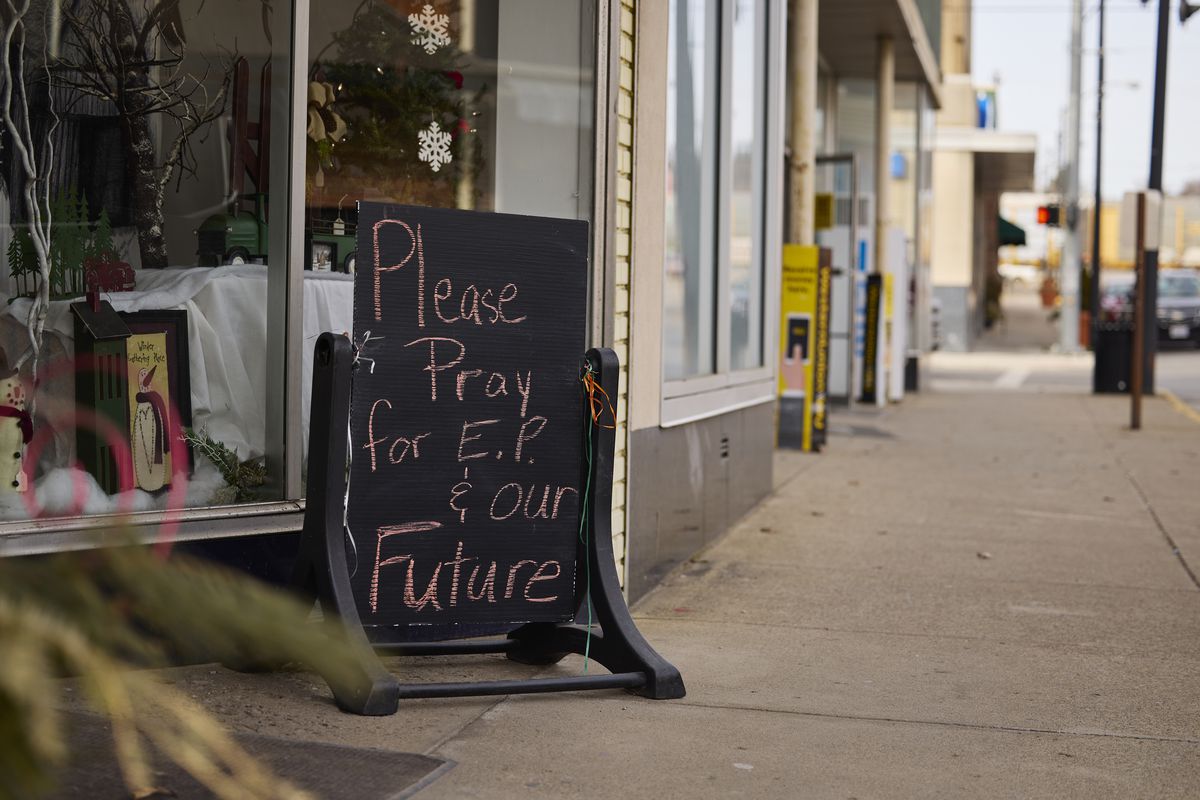 A handwritten sign reading “Please pray for E.P. &amp; our future” is on display outside a flower shop.