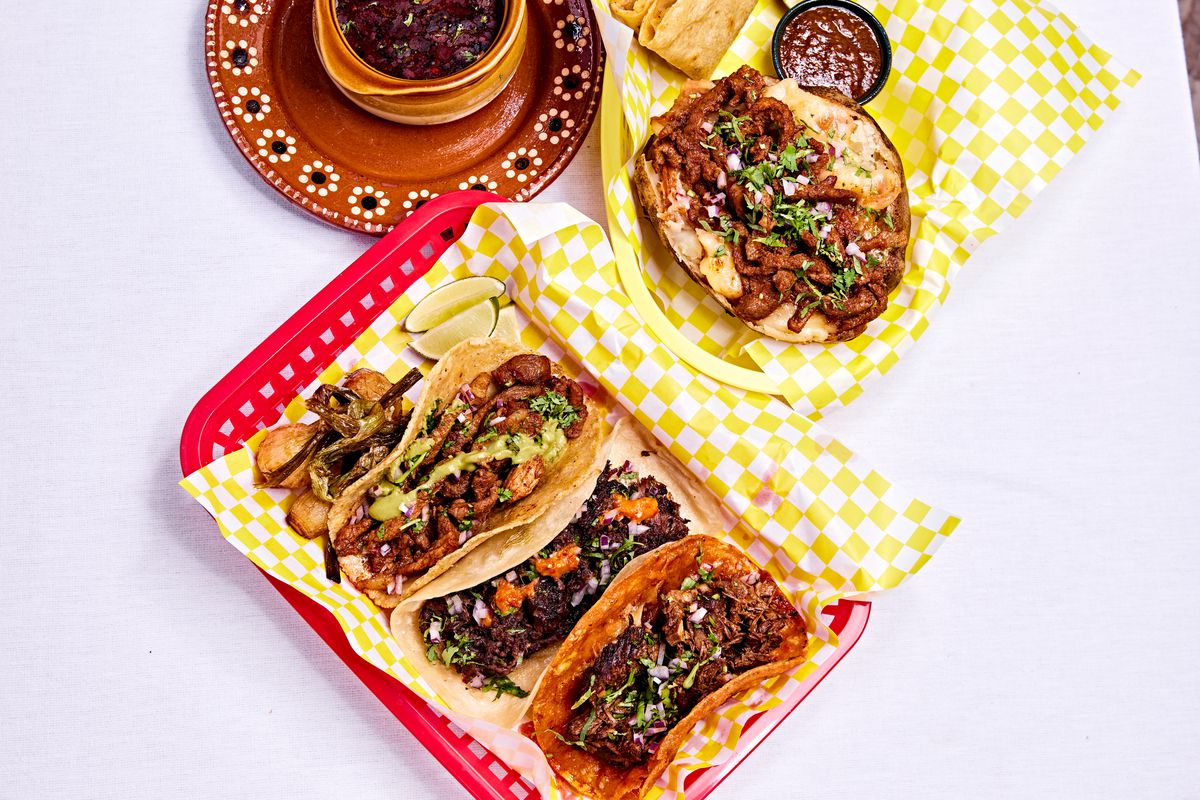 A red tray lined with yellow-and-white-checkered paper with four tacos next to a similar paper with an open sandwich.