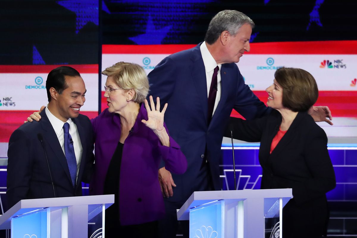 Elizabeth Warren and Julian Castro embrace as Bill de Blasio and Amy Klobuchar greet one another on the debate stage.