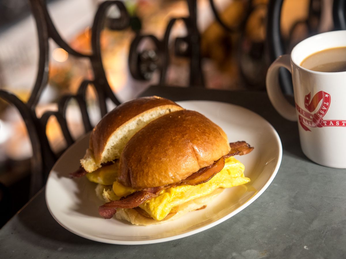 A dramatically lit egg breakfast sandwich beside a mug of coffee