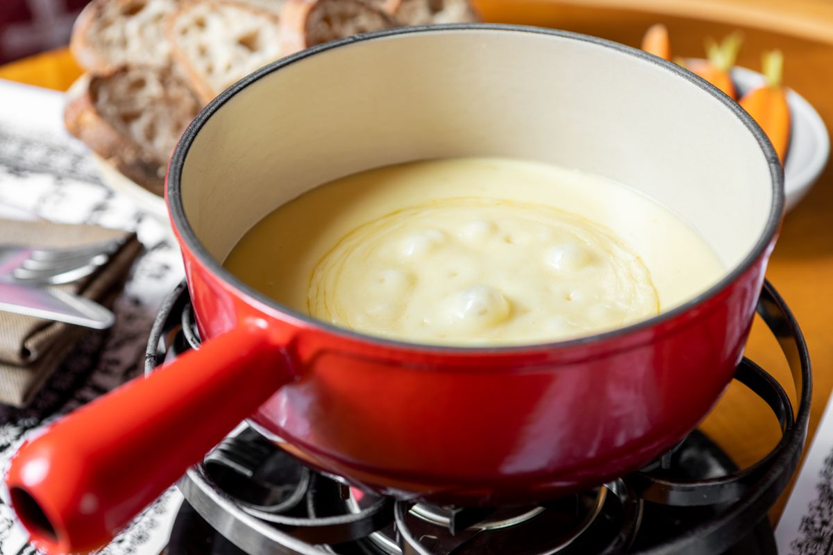 A red fondue pot with bubbling cheese