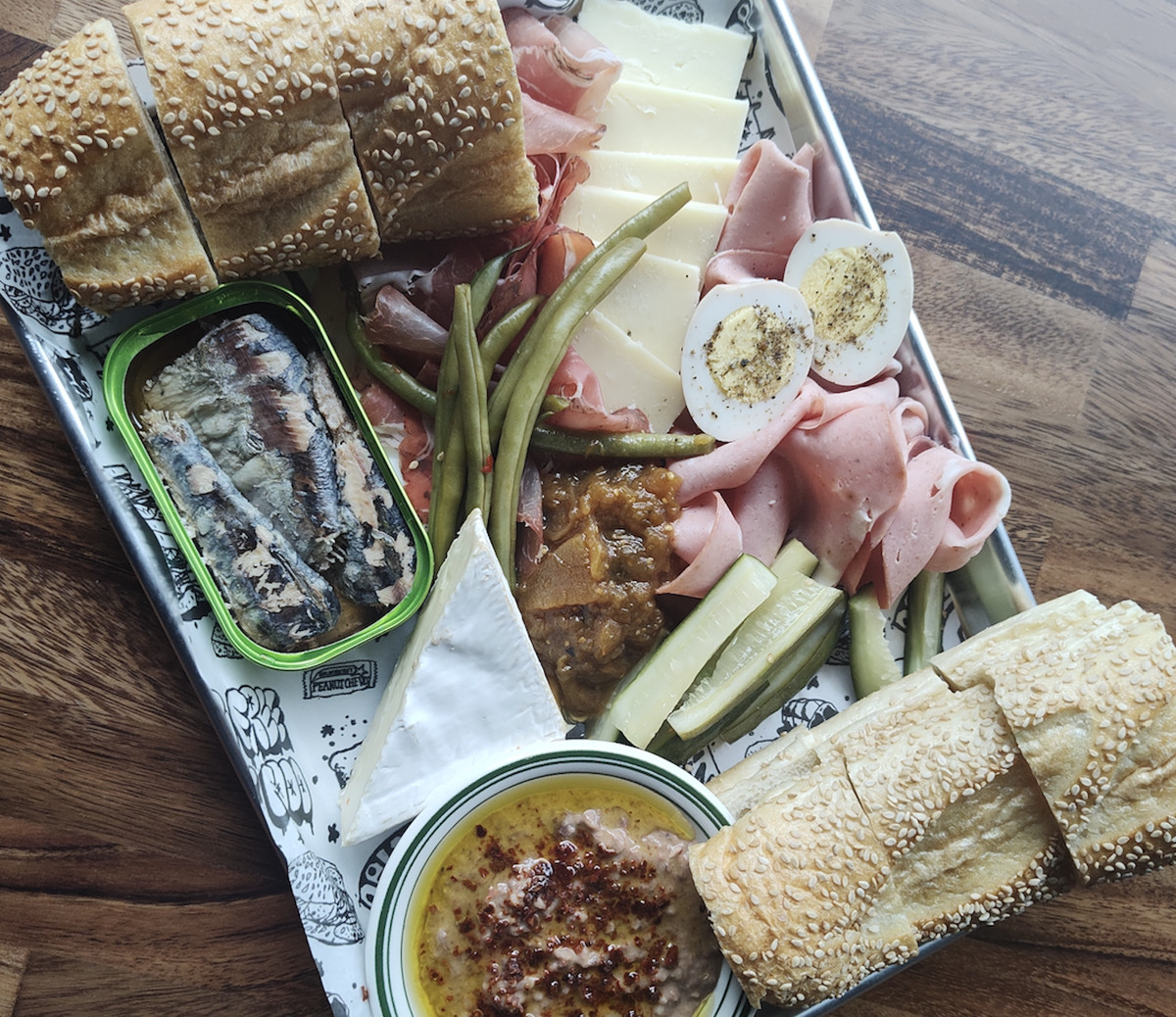 A platter with meats, cheeses, tinned fish, pickles, and bean dip.