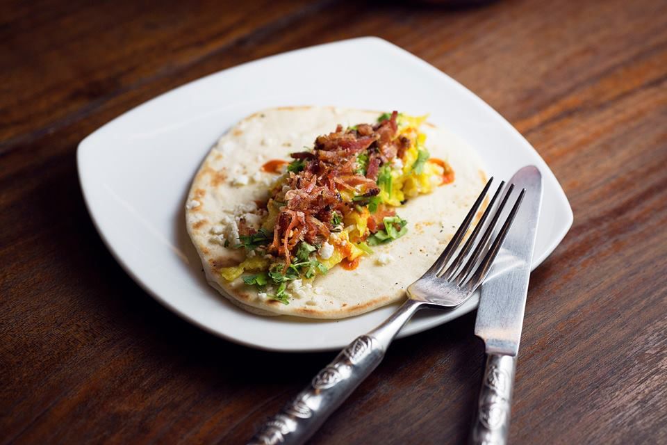 An open-faced flour tortilla topped with bacon, guacamole, eggs and other breakfast fillings