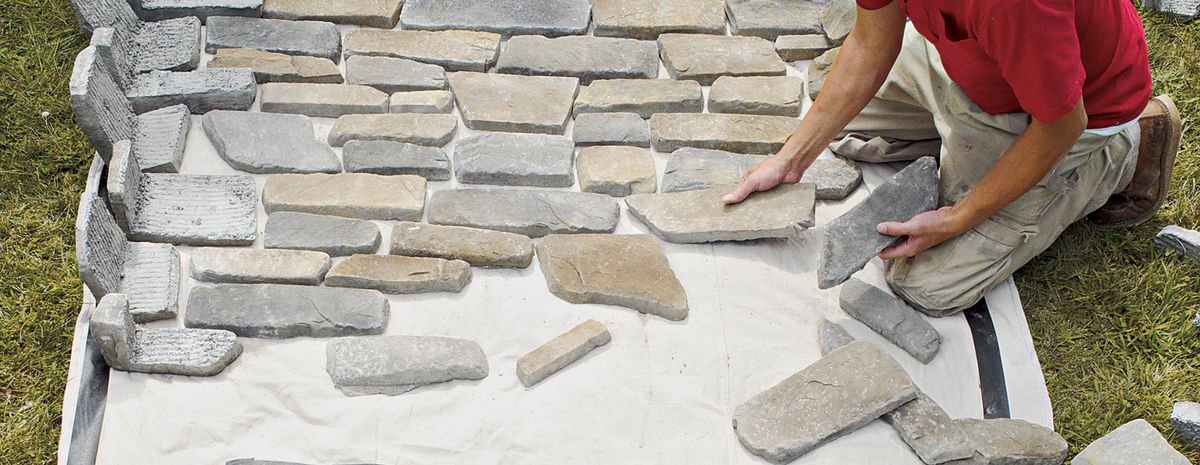 Person laying out many different stones on the floor to prepare for DIY stone fireplace.