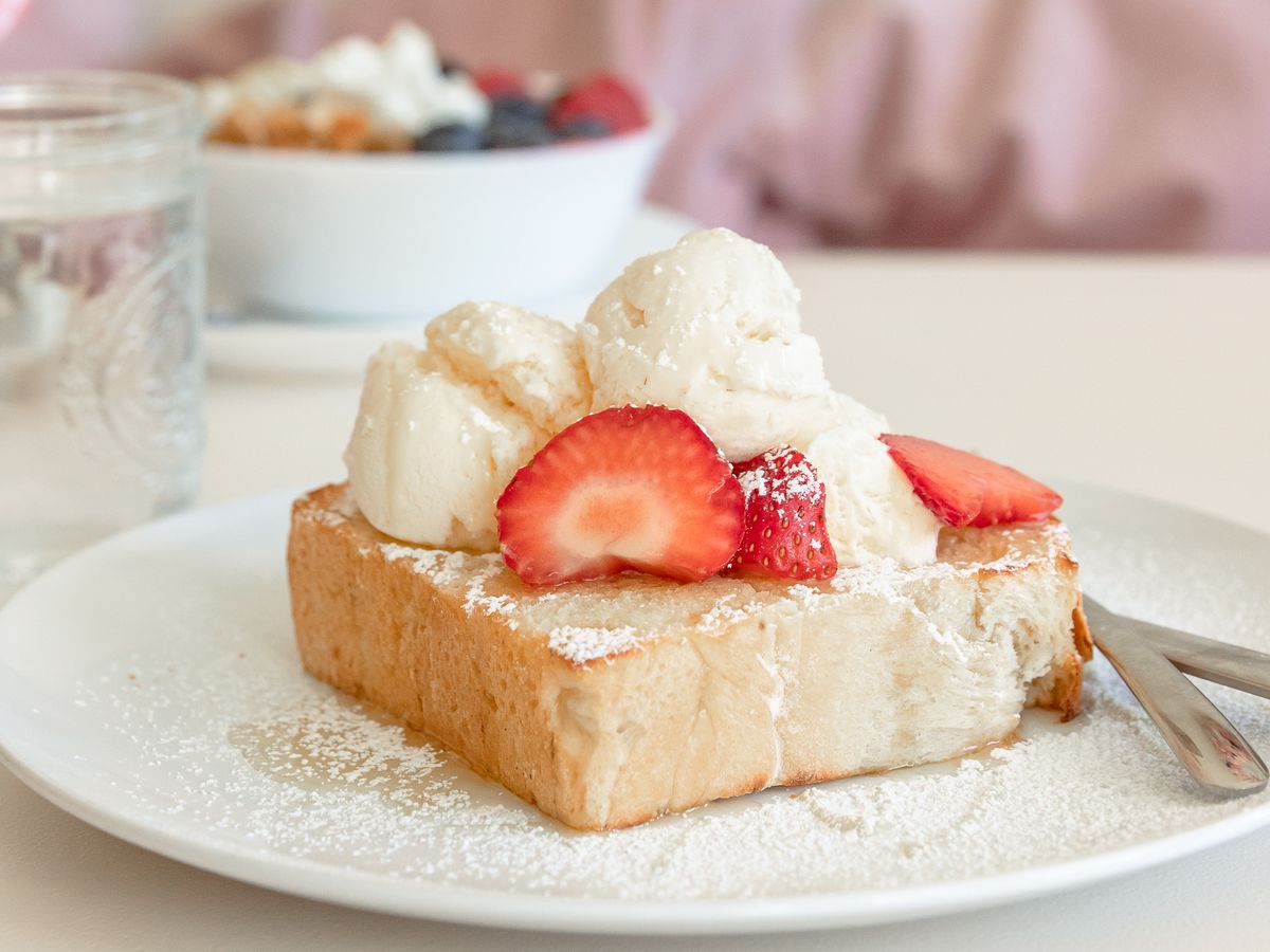Thick slice of white bread topped with ice cream, strawberries, and a drizzle of honey