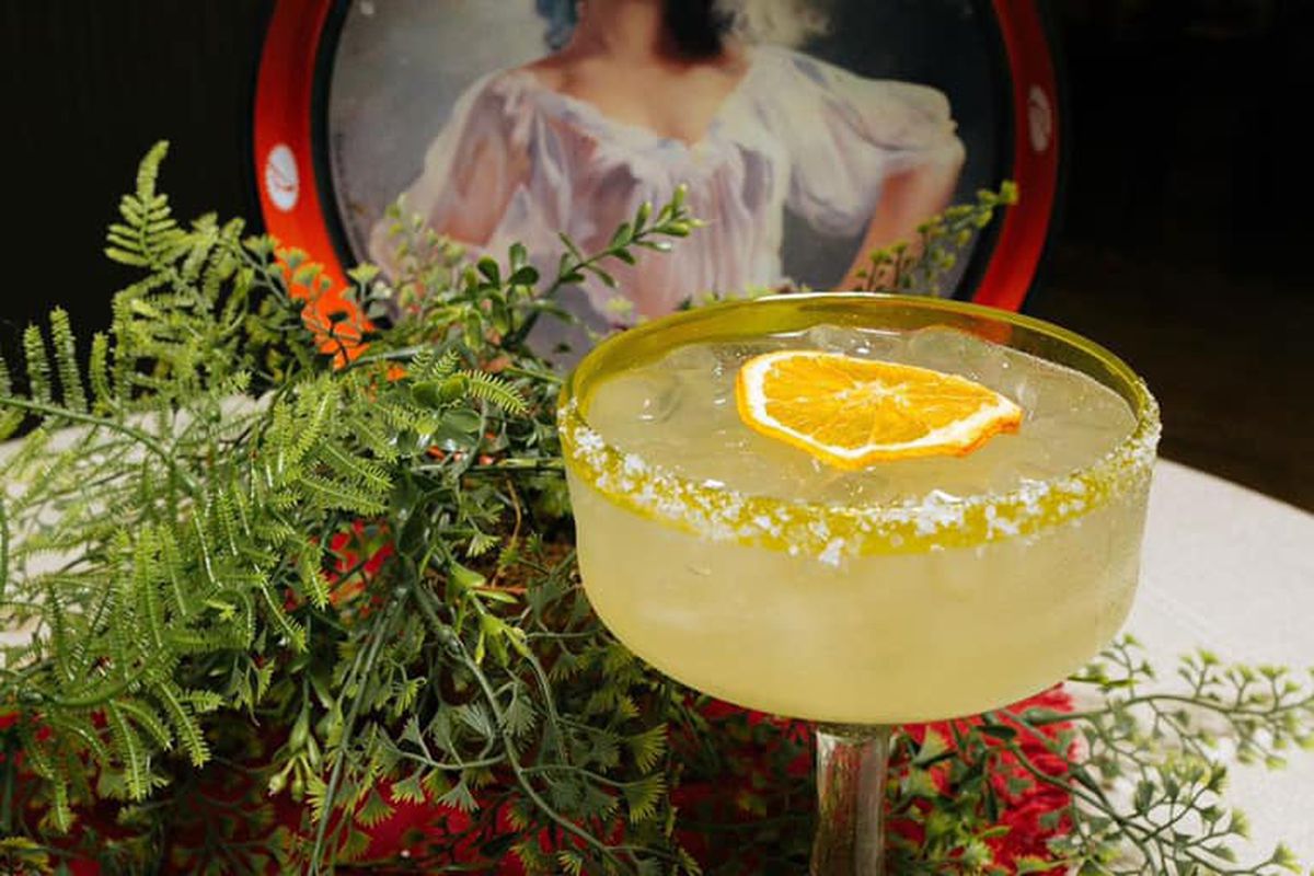 A margarita with an orange wheel garnish in front of a picture of a senorita