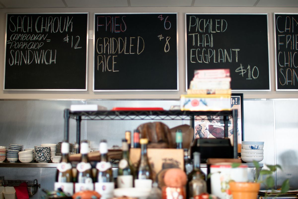 A row of blackboard menus behind a crowded shelf inside a restaurant.