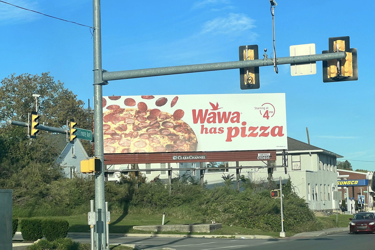 A large billboard in the daytime that shows an image of a pizza and marketing. 