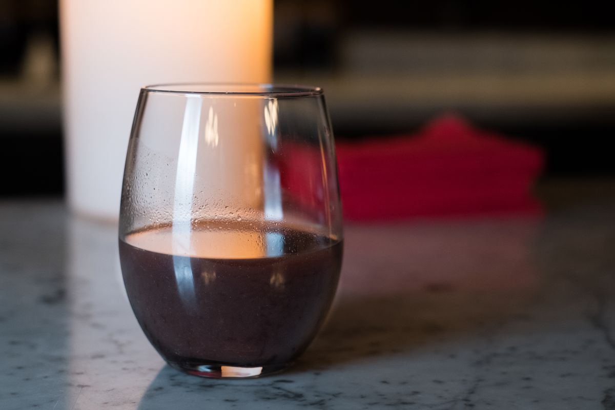 A dark colored liquid in a low, stemless wine glass on the stone-topped bar