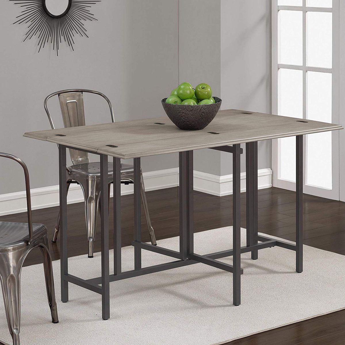 A compact dining room table has steel legs, a wooden gray top, and two metal chairs. All are sitting on a beige rug. 
