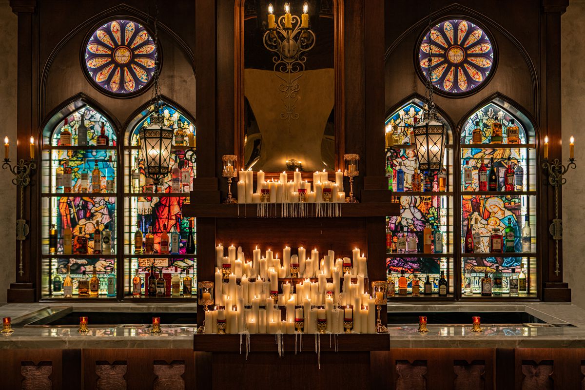 Stained glass windows behind the bar at Sinners y Santos in Downtown LA with candles with liquor bottles.