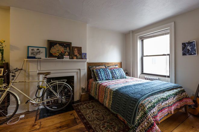 A living area with a bed that has patterned bed linens, a fireplace, a bicycle, and a window.