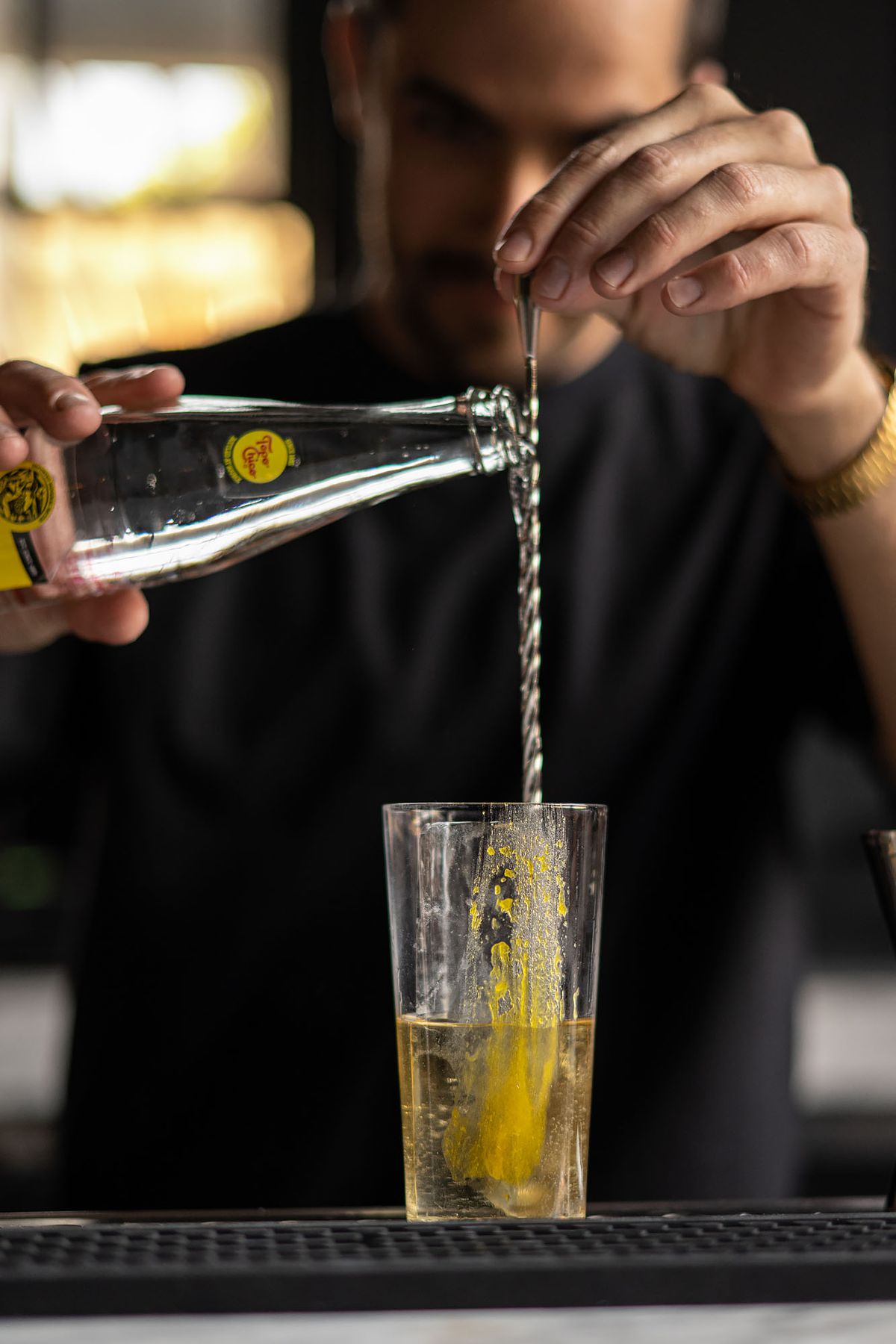 A bartender pours seltzer into a tall glass.