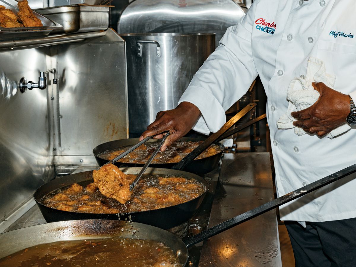 A man, chef Charles Gabriel, plucks a piece of fried chicken from a stainless steel pot of bubbling oil.