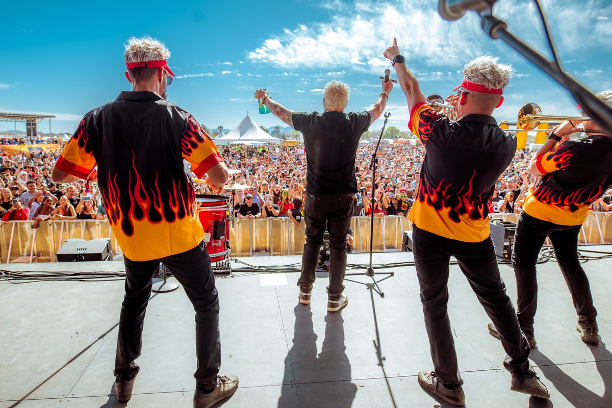 A trio of Guy Fieri impersonators perform on stage at Guy’s Flavortown Tailgate.
