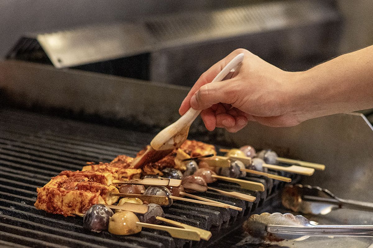 Several meat skewers on a grill being brushed with sauce.