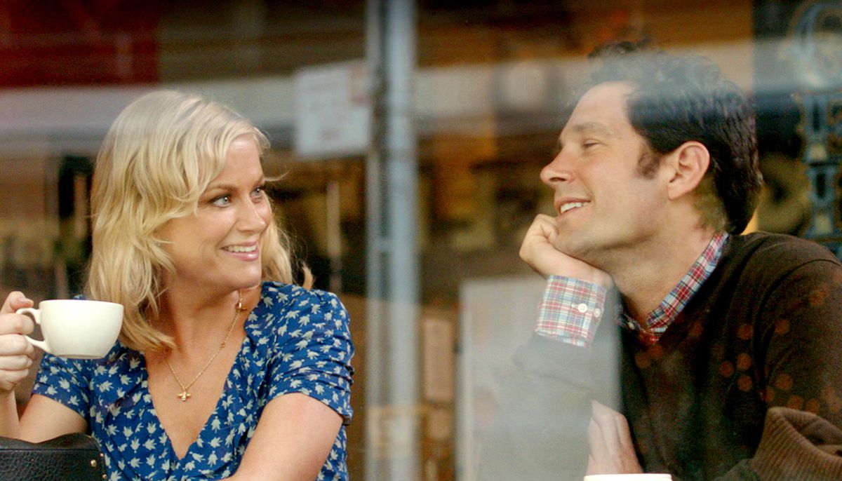 Amy Poehler and Paul  Rudd smile at each other in the window of a coffee shop in They Came Together