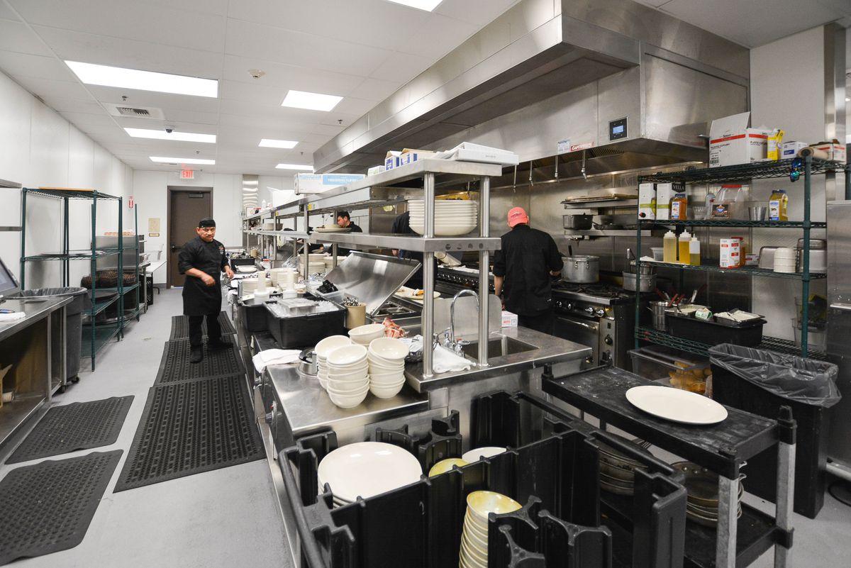 Workers in a bright kitchen, wearing black cook shirts.