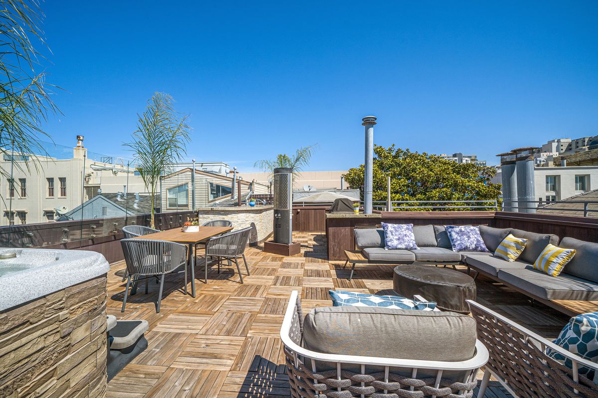 A rooftop deck with crosshatched wooden flooring, a hot tub, and an L-shaped patio sofa.
