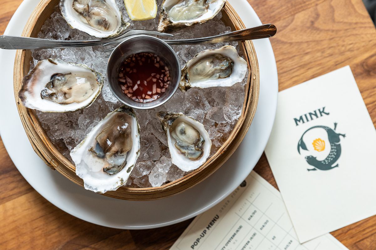 A tray of oysters on ice next to a menu for Mink.