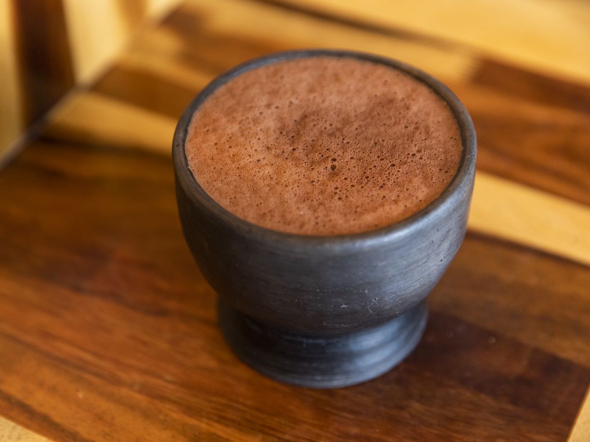 A frothy cup of drinkable chocolate in a black clay mug on a wood tabletop