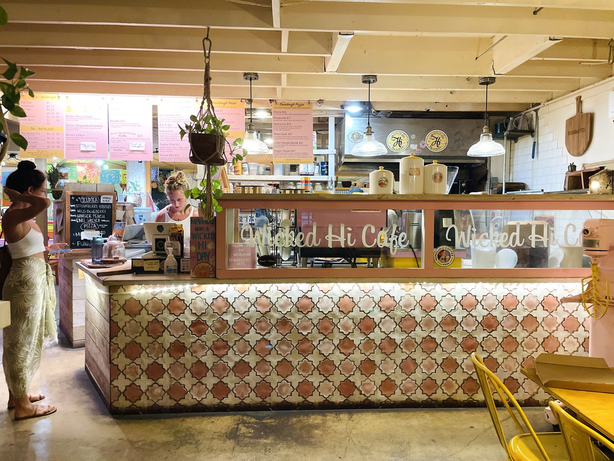 A cafe interior with loud textured wallpaper, white wood beam ceilings, and a pastry case scrawled with the name of the cafe. 