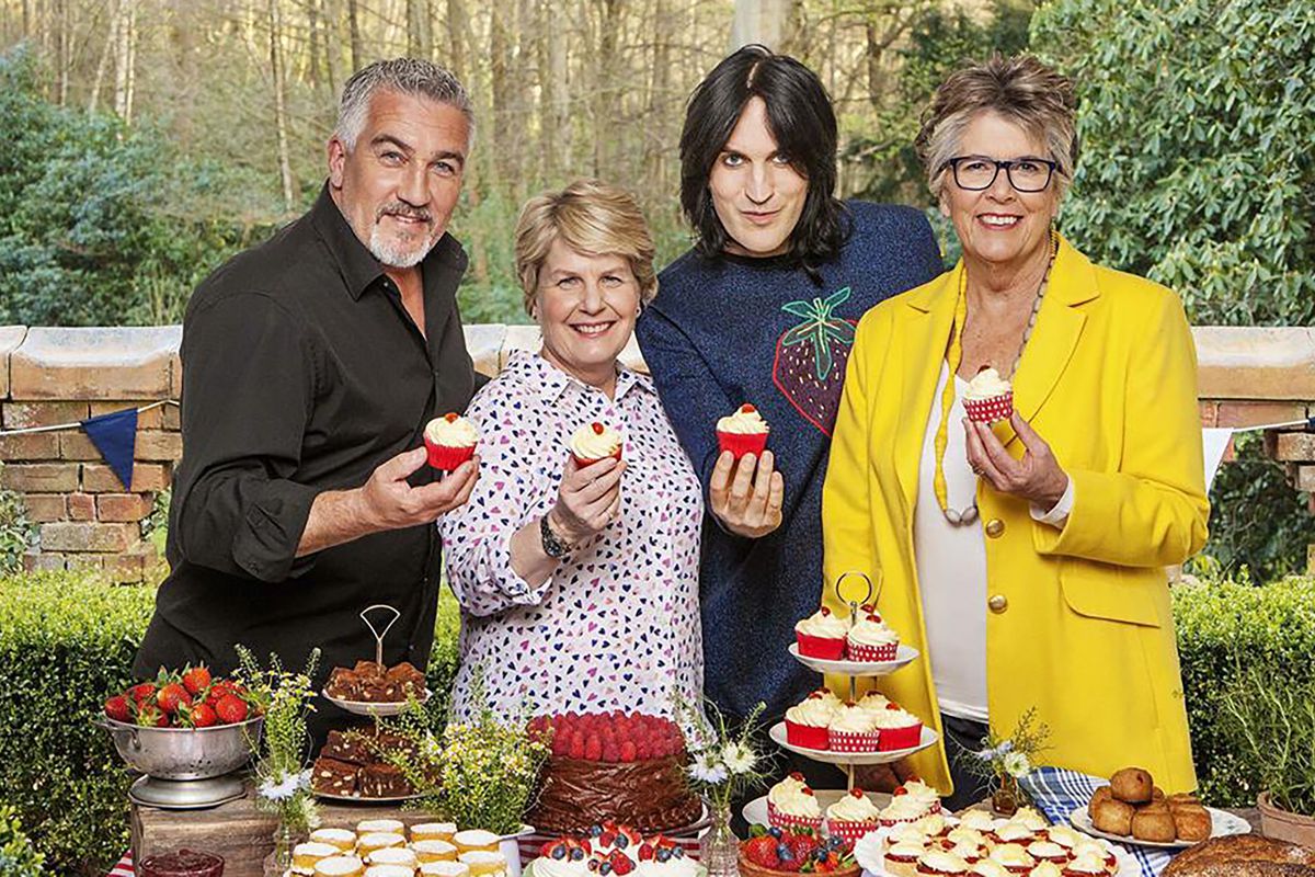 Paul Hollywood, Sandi Toksvig, Noel Fielding, and Prue Leith stand in front of a table filled with pastries holding up cupcakes with cherries on top.