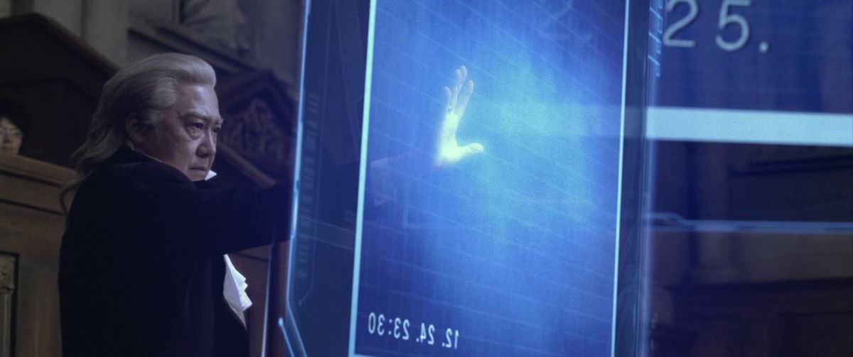 Un fiscal extiende su mano para tocar una pantalla holográfica gigante en la adaptación de acción en vivo de Ace Attorney.
