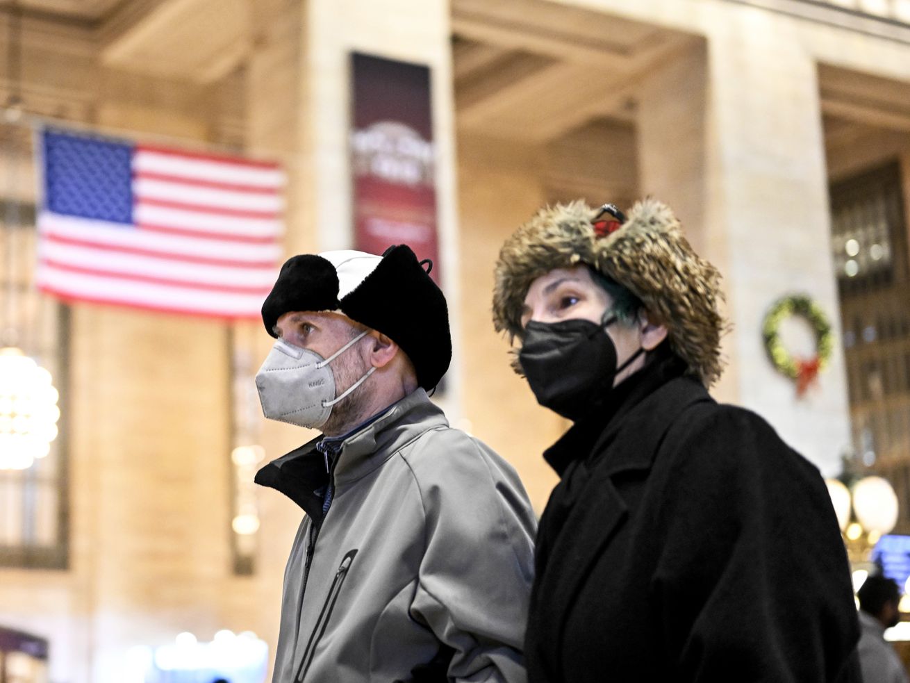 Masked pedestrians walk past a US flag in a streetfront window in New York City on December 12, 2022.
