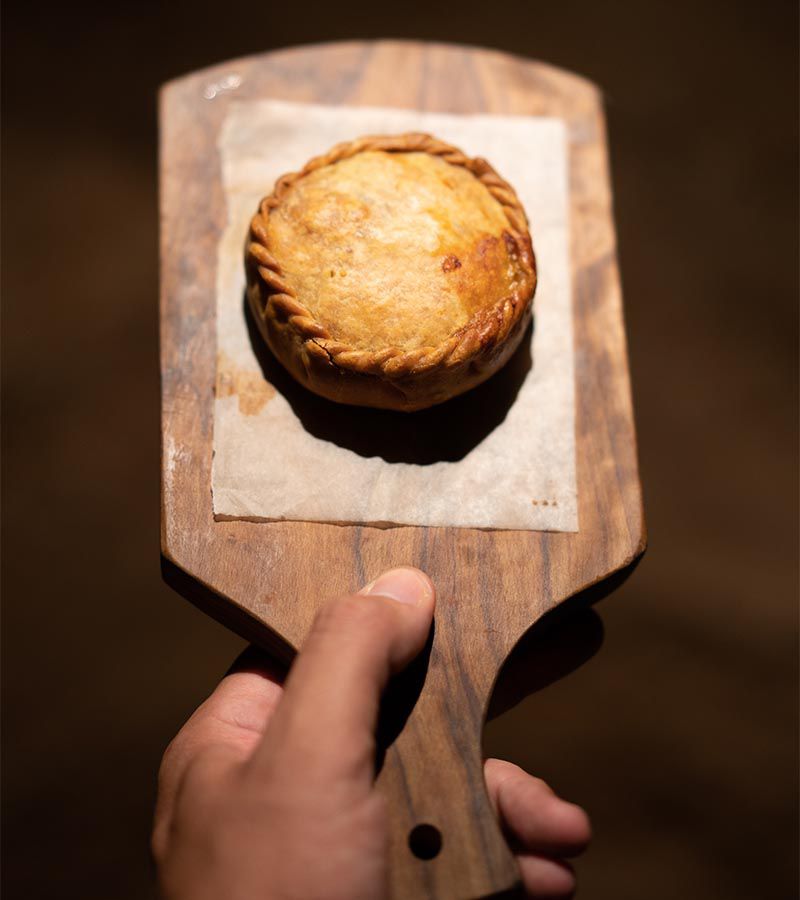 A neatly crimped pastry served on a wooden plank