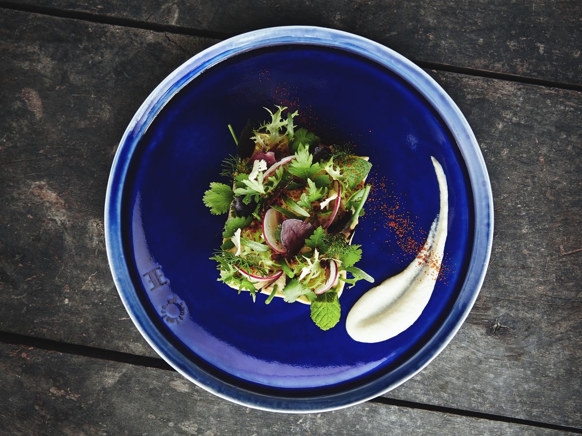 From above, a vibrant green dish topped with herbs presented on a deep blue plate.