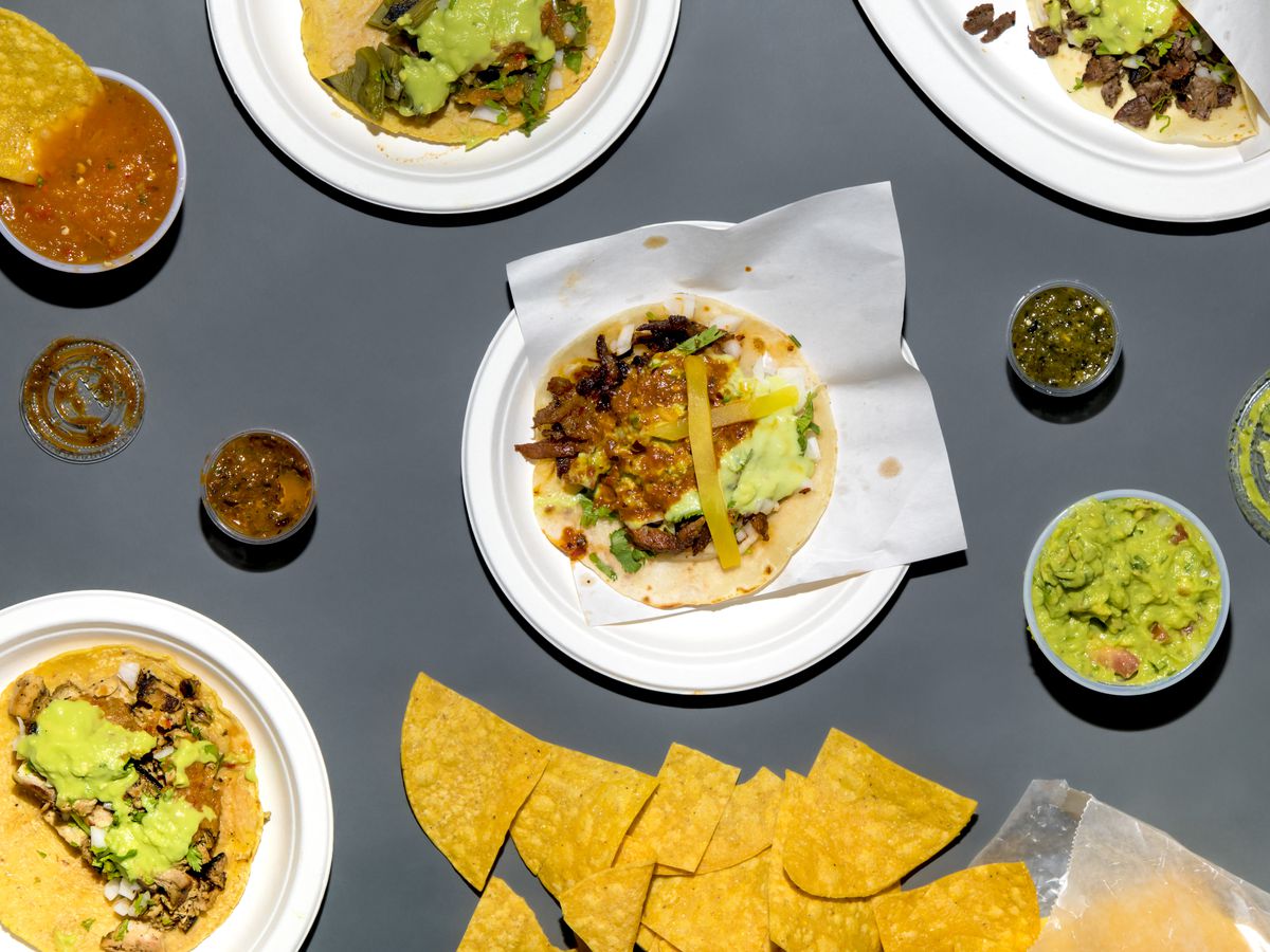 An overhead photograph of tacos, chips, guacamole, and plastic sides of salsa.
