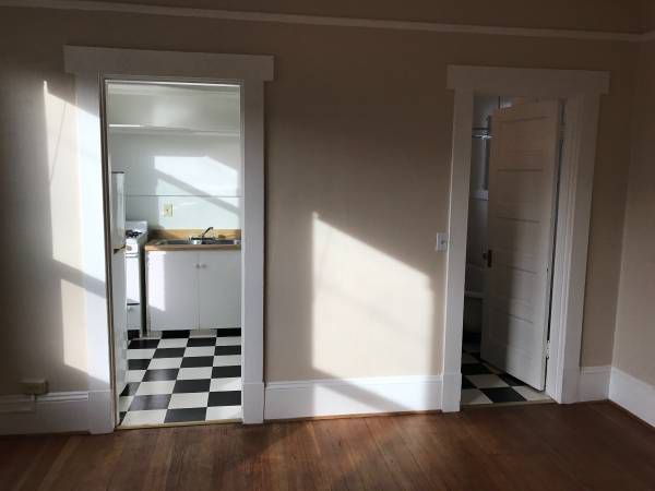 Two doors viewed from a room with a hardwood floor. Both rooms the doors lead to have black and white checkered floors. The door to the left leads to the kitchen.