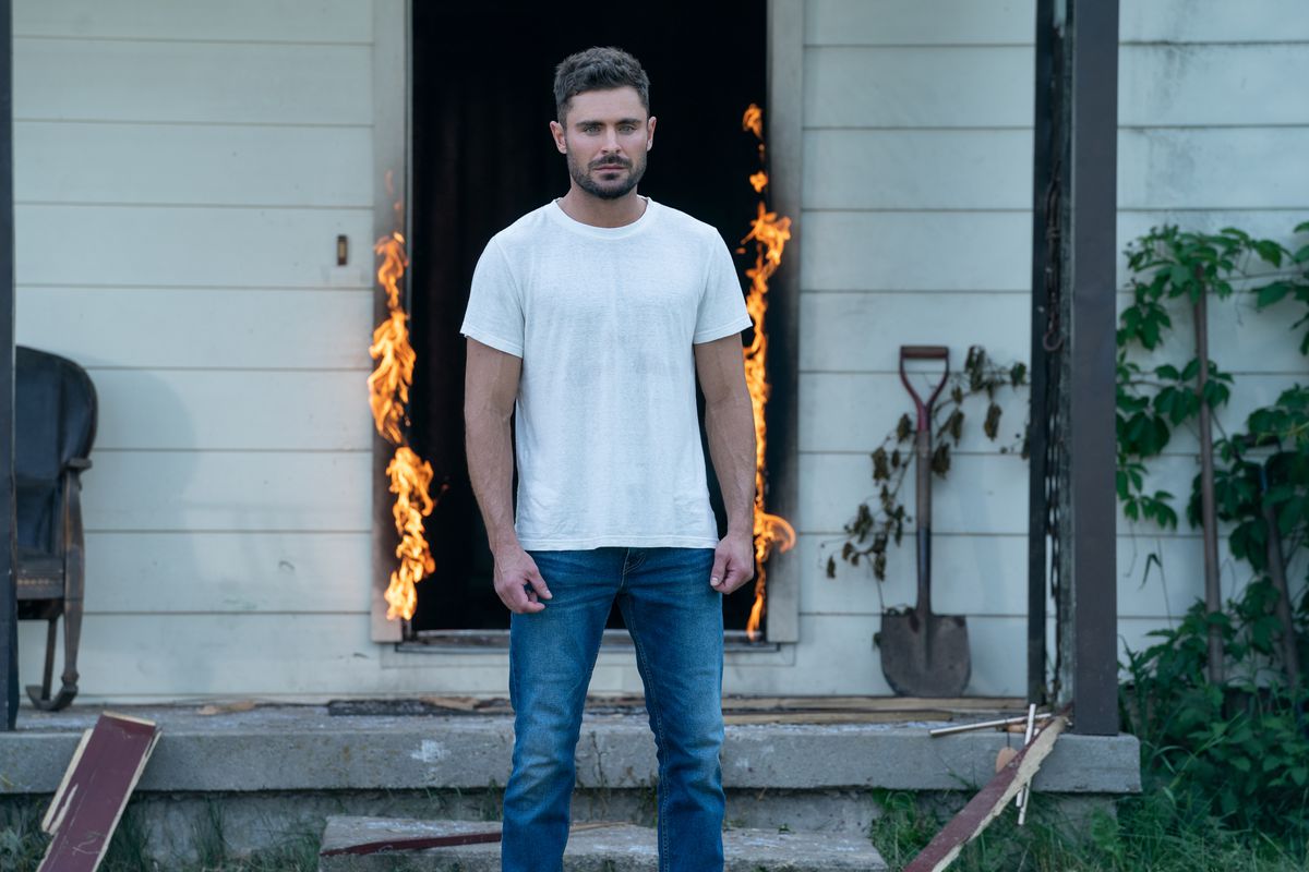 Zac Efron on Firestarter, standing outside in front of a house with an open and burning doorway