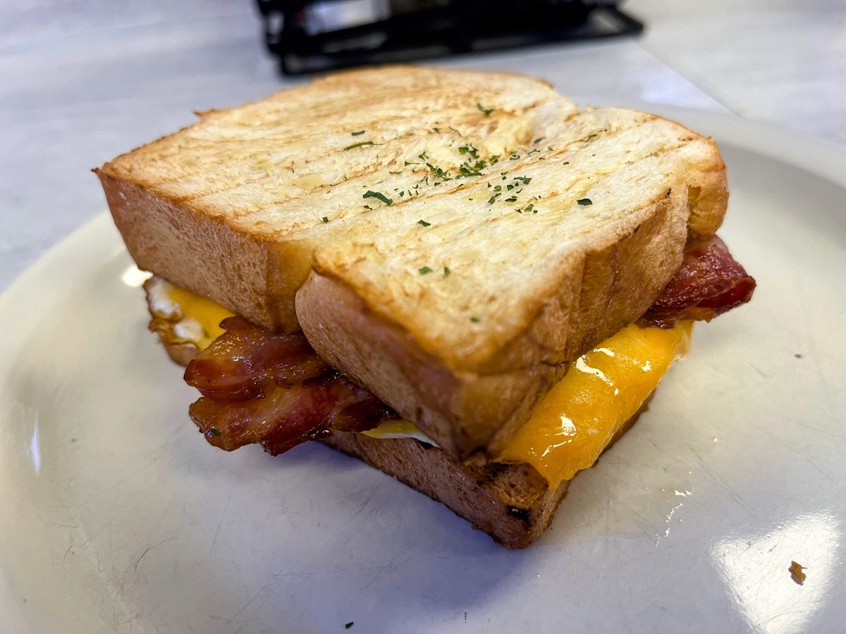 A toasted white bread sandwich with bits of bacon and cheese peeking out of the sides.
