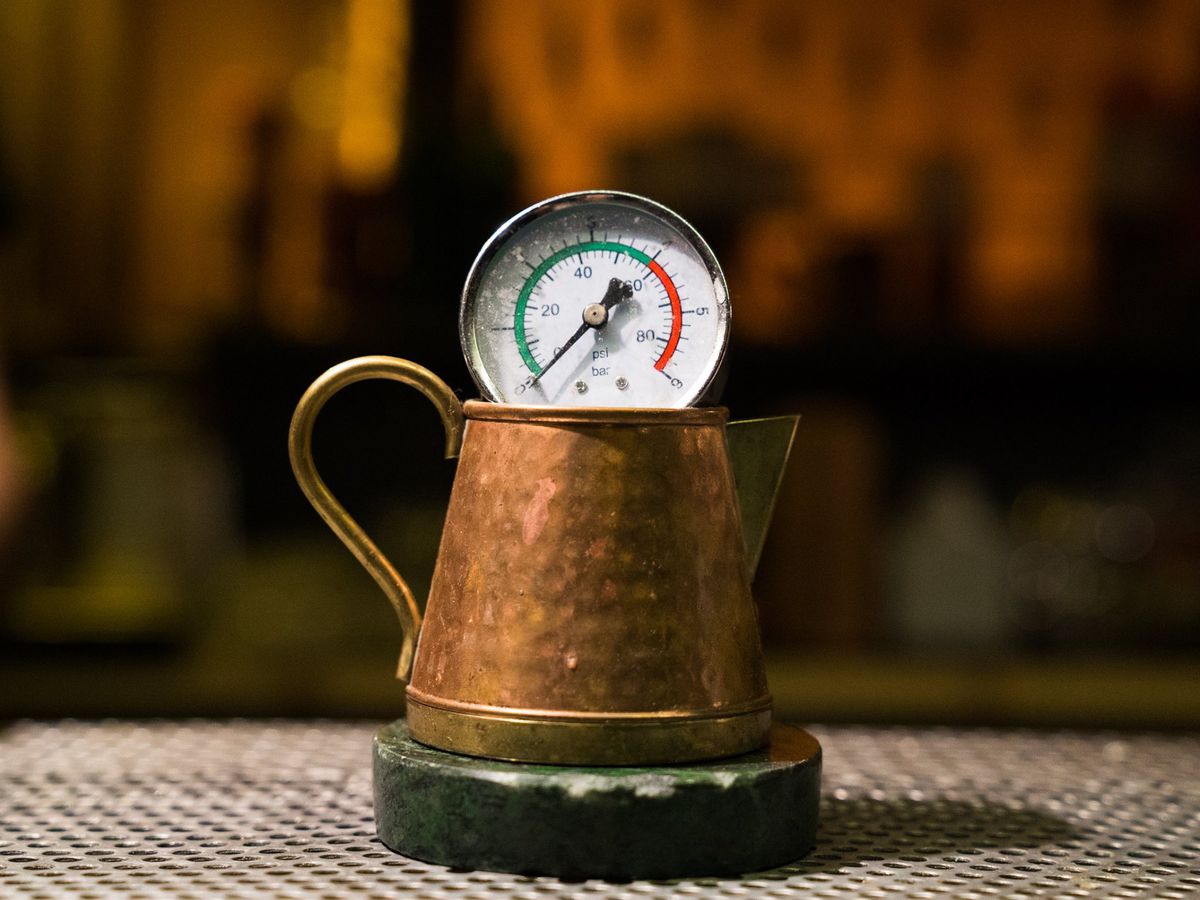 A copper saucer sits on a coaster with a pressure gauge sitting across the rim in a darkened bar setting
