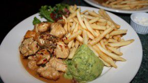 A white plate with chicken, guacamole, and french fries