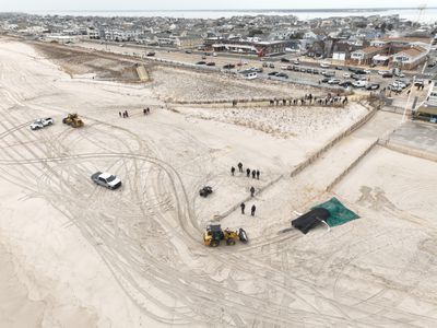 An aerial shot of a beach. Tarp covers the body of a whale surrounded by a people and construction vehicles.