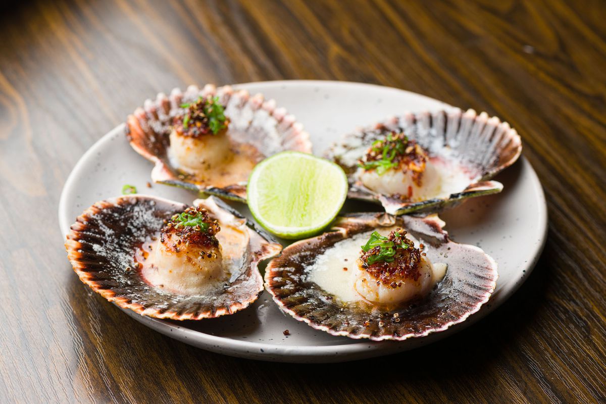 A side shot of grilled scallops and lime on a wooden table.