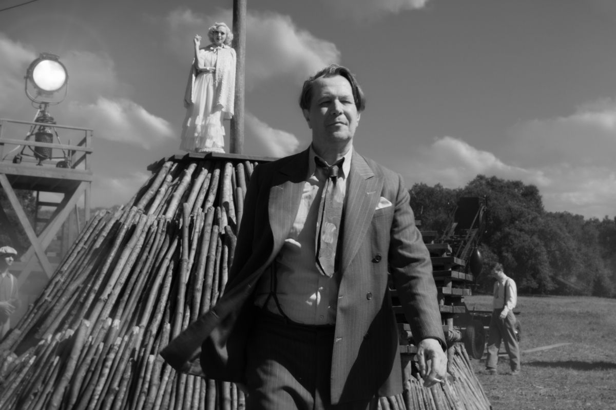 A black-and-white image of a man striding away from a movie set, an actress standing atop a pyre in the background.