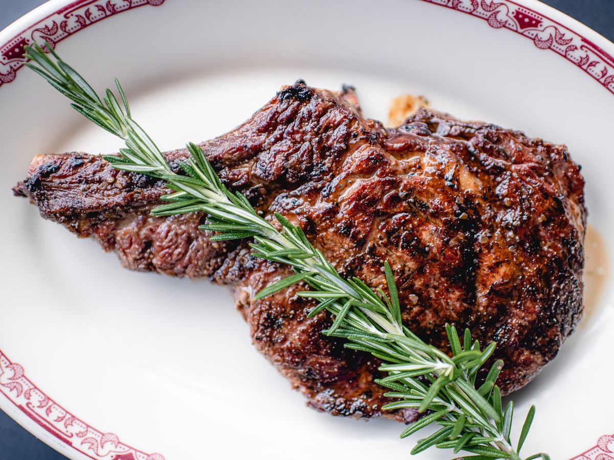 A ribeye beef steak with a sprig of rosemary on top.
