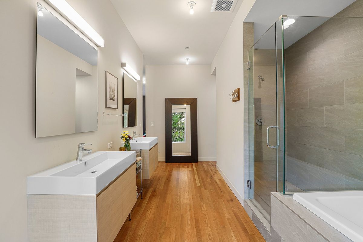 A roomy bathroom with two rectangular sinks mounted on the wall beneath square mirrors and lights. 