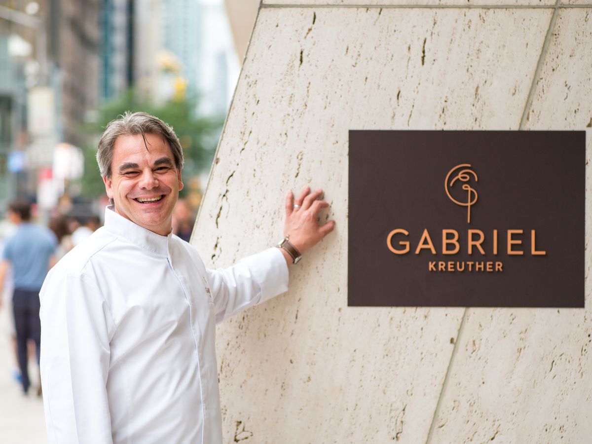 Gabriel Kreuther stands in front of a sign that says the name of his restaurant.