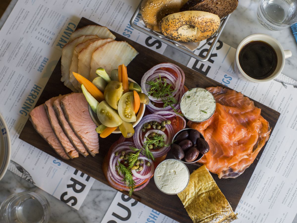 A wooden board covered in smoked fish, cream cheese, and pickled vegetables